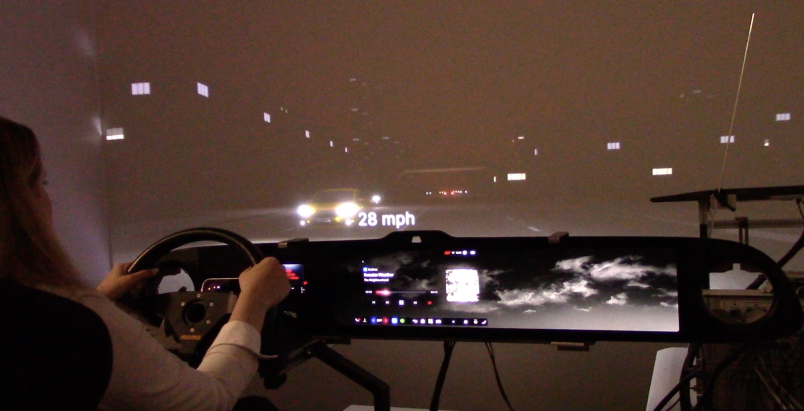 A participant drives a physical seat buck against a projected night-drive; the outpaint runs live on the head unit.